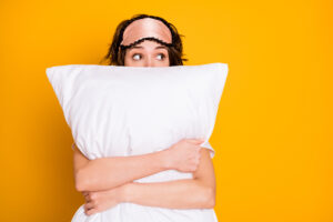 A women with an eyeshade pushed up her head hugs a large pillow
